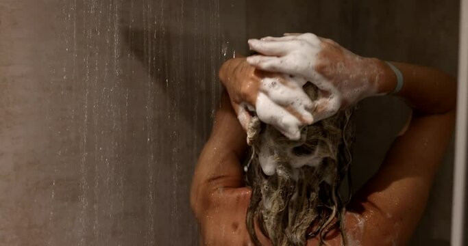 Woman washing hair with shampoo in shower with hair care. Girl uses rinsing shampoo and balm