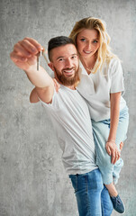 Cheerful man holding wife and smiling while showing apartment keys. Happy couple real estate house buyers demonstrating keys from new home.