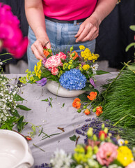 Florist arrangiert bunte Blumen in einem Gef&auml;&szlig; aus Keramik, Blumengesteck mit frischen Blumen, 