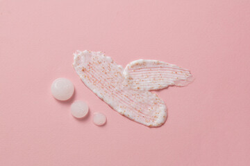 White exfoliation cream smear smudge sample decorated on pink background. Few drops in milky white color displayed beside