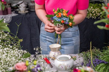 Florist bei der Arbeit, Frau bindet frische Blumen zu einem kleinen Strauß mit Rosen, Prärieenzian, Margeriten, Sterndolden, Klematis, Kamille und Hortensien