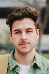 Vertical close up portrait of confident teenage male student looking serious and relaxed at camera in a college. Handsome caucasian guy standing in university campus with pensive expression. High