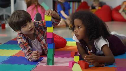 Cute multiethnic preschool kids playing with colored blocks on floor at nursery school