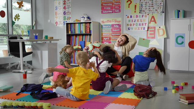 Group of elementary students exercising with teacher sitting on floor in classroom