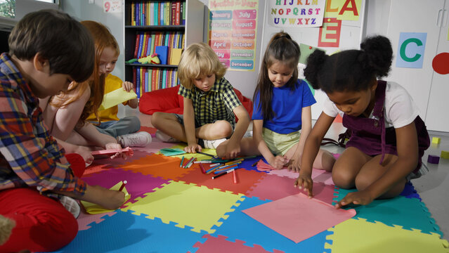 group of preschool children draw in classroom sitting on floor