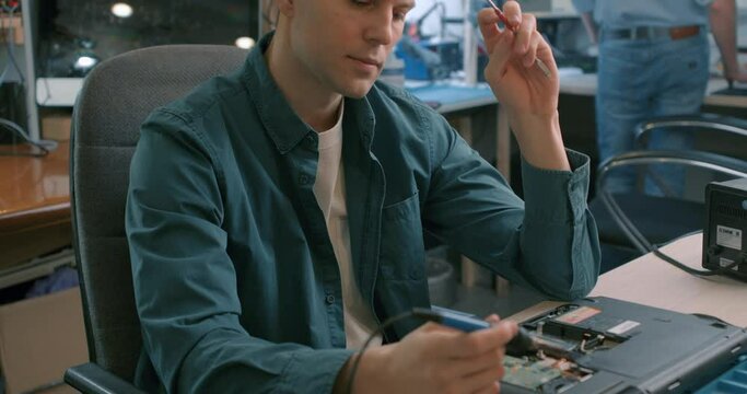 Electronic renovation.skilled talented blonde repairman tinkering computer detail, Slow motion Repairman beginner tries to fix a problem in electronic device with soldering iron on the table