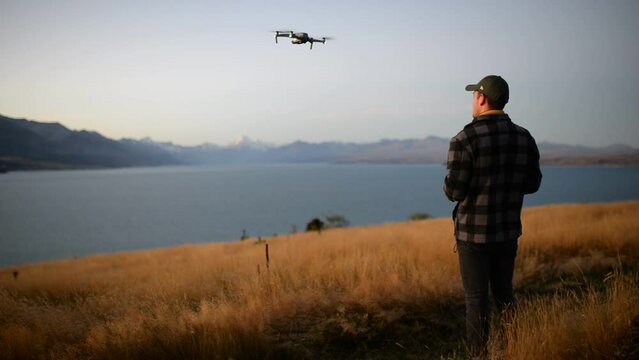 Young man starting to fly a modern drone from hand in front of a lake in New Zealand