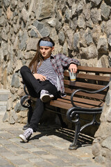 Long haired man sitting on bench with glass of drink