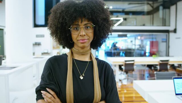 Young beautiful African-American businesswoman posing with arms crossed in modern open space office during working day. Video portrait, medium shot