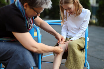 Grandmother sticks a bandage on the child's wound on the playground.