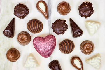 chocolate pieces from various type in box for valentine's day with small glitter heart on marble background