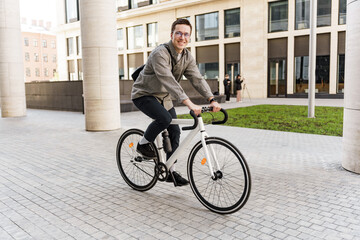 A happy entrepreneur guy with a business bag uses environmentally friendly transport. A man in formal attire is smiling on a bicycle and has arrived at work career in the office.