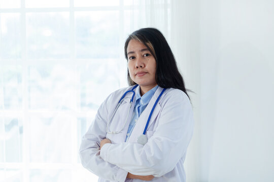 Portrait of a female doctor wearing a white medical coat and stethoscope head standing with arms crossed looking at the camera on a white background.