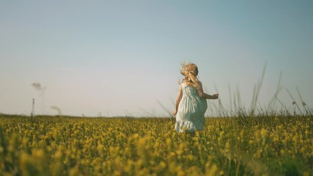 Sweet blond little girl running in blooming flower field during sunset time in nature - Low angle following shot in slowmotion