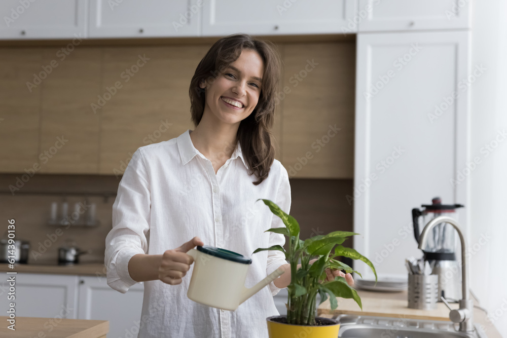 Wall mural young housewife holding can watering houseplant in pot, smile looking at camera, take care of green 