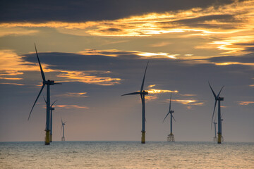 Obraz premium Fans of wind turbines spin over the sparkling sea. Dynamic clouds at sunset. An offshore wind farm off the northwest coast of Taiwan. One of green power.