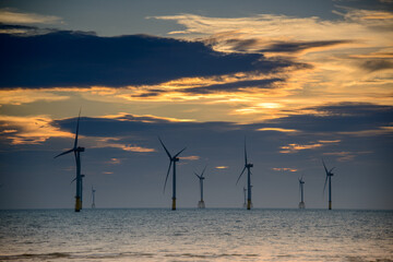Fans of wind turbines spin over the sparkling sea. Dynamic clouds at sunset. An offshore wind farm...