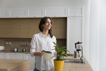 Dreamy happy woman watering succulent houseplant from cane, look aside. Female florist taking care...