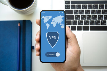 male hand holding phone with app vpn laptop in office