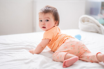 lifestyle home portrait of happy and beautiful 8 months old baby girl mixed race Asian Caucasian playing cheerful on bed exploring the surroundings curious