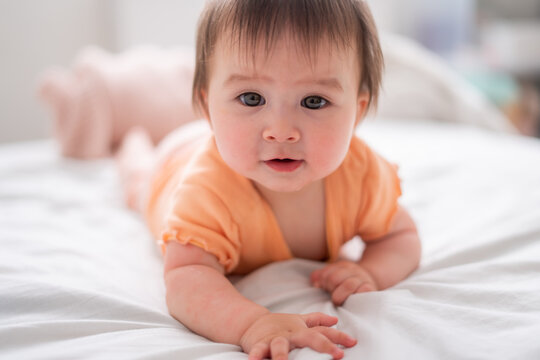 lifestyle home portrait of happy and beautiful 8 months old baby girl mixed race Asian Caucasian playing cheerful on bed exploring the surroundings curious