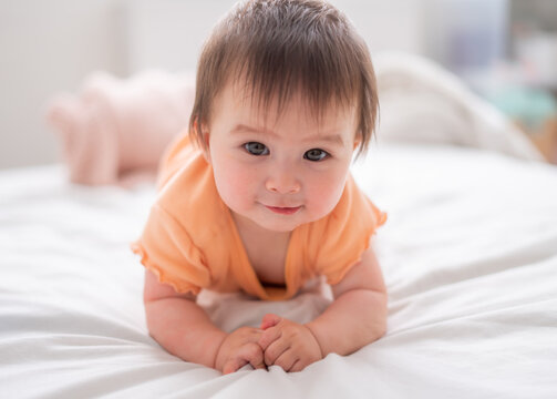 lifestyle home portrait of happy and beautiful 8 months old baby girl mixed race Asian Caucasian playing cheerful on bed exploring the surroundings curious