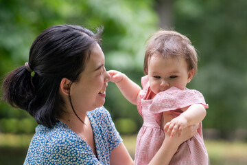 outdoors lifestyle portrait of mother and daughter - young happy and sweet Asian Korean woman playing with her 8 months baby girl at city park