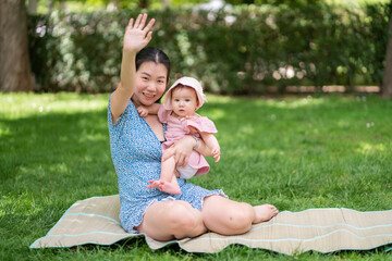 Fototapeta premium outdoors lifestyle portrait of mother and daughter - young happy and sweet Asian Korean woman playing with her 8 months baby girl on grass at city park