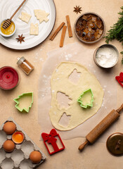 Process of making Christmas cookies with homemade dough,cookie cutters in the shape of tree and gift box,rolling pin,flour,cinnamon,cocoa powder and fresh eggs on beige table.Top view.