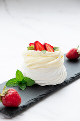 Pavlova meringue cake with fresh straberry and whipped cream mascarpone with mint leaf decoration served on black rock board. Recipe of traditional dessert Anna Pavlova. Confectionery cafe menu.