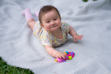 Fototapeta premium adorable and happy baby girl hat embraces the joys of playfulness on a soft blanket playing with little toy. Laughing as she explores the natural wonders of an outdoors city park