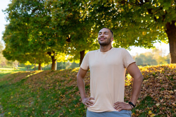 Smiling sportsman resting in the park on a run, man breathing fresh air enjoying an active lifestyle, hispanic man exercising. - obrazy, fototapety, plakaty
