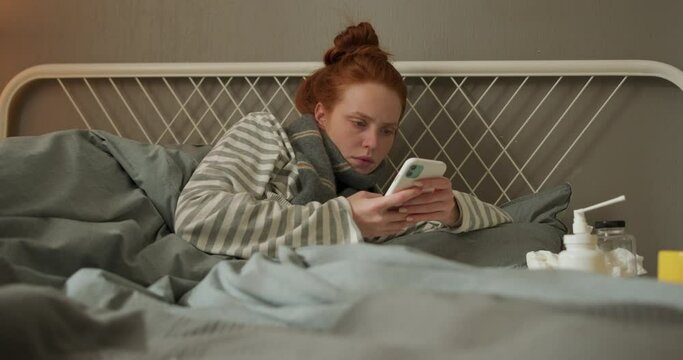 young redhead sick female patient making phone call to a doctor on cellphone medical app in telehealth telemedicine online service hospital quarantine social distance at home. girl browsing the net