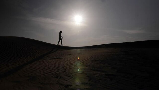 Silhouette of Middle eastern man wearing a turban walking in desert sunset over sand dunes in middle eastern desert landscape near Dubai in the United Arab Emirates.