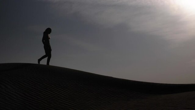 Middle eastern man in desert wearing turban walking across sand dune in sunset. Middle eastern desert landscape near Dubai in the United Arab Emirates.