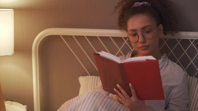 awesome young woman enjoying reading process before falling asleep. close up portrait, rest time, slow motion daily routine hobby interests