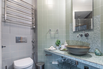 The elegant interior of the bathroom, decorated with various tiles. The bowl of the sink on the countertop made of mosaic tiles. Stylish accessories.