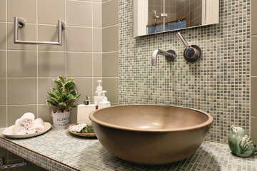 Stylish bathroom design. Modern sink bowl on the countertop decorated with mosaic tiles. Hygiene products, towels, potted houseplant.