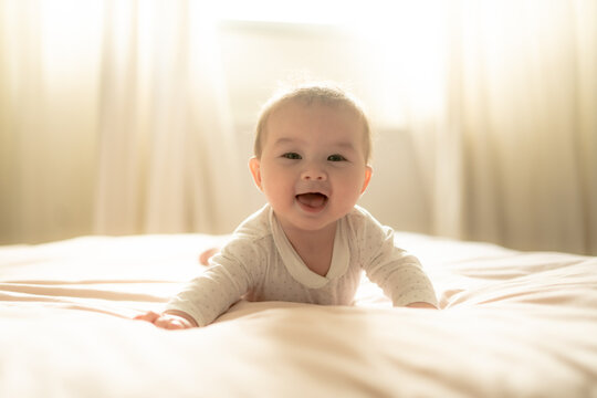 adorable and happy 5 months old baby girl gleefully discovers boundless joy while playfully exploring her bed. Surrounded by the warm glow of natural light the little on smiles cheerfully