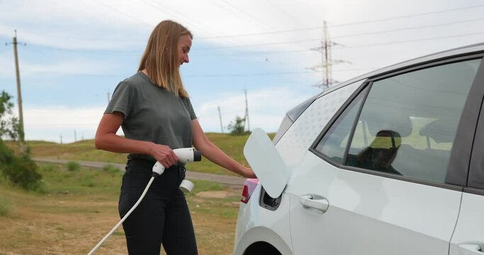 Mature woman plugging electric charger into car outdoors