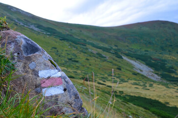 Red tourist route marker on a stone high in the mountains. A tricolor flag with two white stripes and one red stripe. Hiking trail marking.