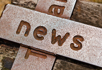 A detail of a stone with the carved word NEWS laying on a wooden surface