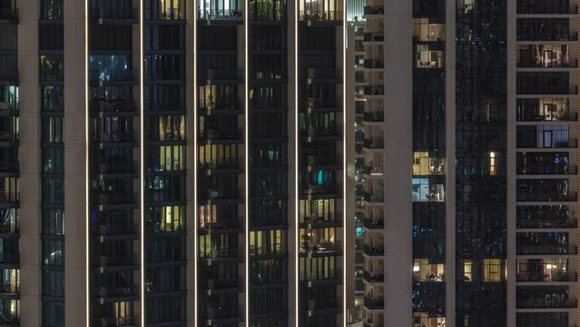 Tall blocks of flats with glowing windows located in residential district of city aerial timelapse. Evening yellow light in rooms in towers and skyscrapers