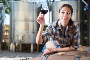 girl examines glass of wine on the background of barrels for fermentation