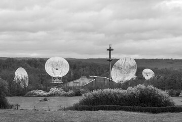 Radio satellite dishes in a natural rural setting against a cloudy overcast sky, in monochrome