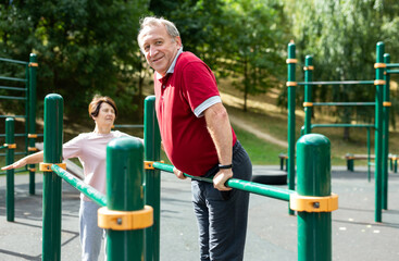 Senior man pulls up on crossbar in city park on sports ground