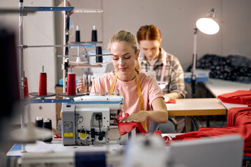 focus on adorable caucasian blonde lady using sewing machine. happy women working as seamstress in clothing factory, clothing production concept. dressmaking, tailoring in workshop