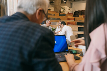 Businesspeople working together at modern co working space. Project manager in grey shirt helping his middle-aged colleagues