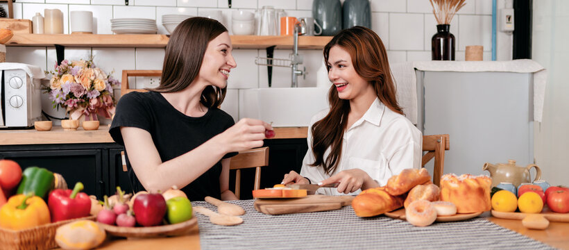 Two young woman spreading jam on slice bread and holding fruit w