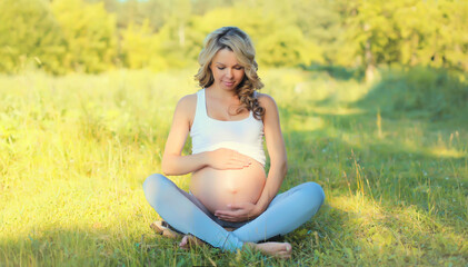 Fototapeta na wymiar Happy young pregnant woman resting sitting on the grass in summer park